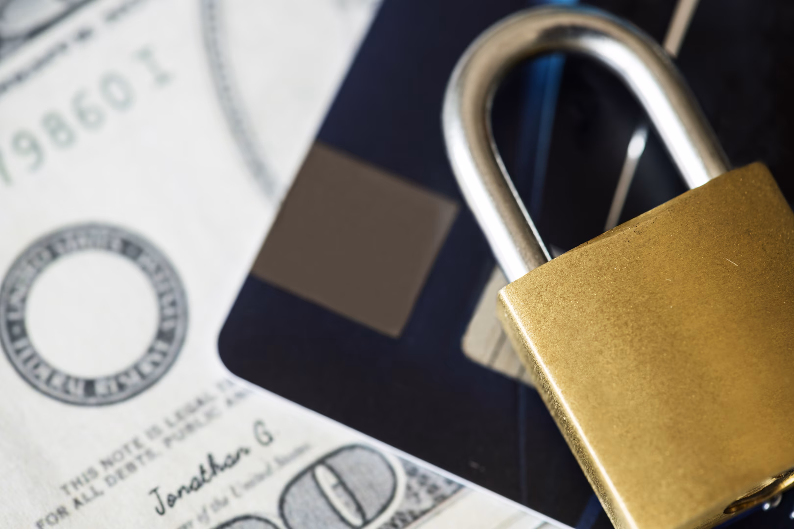 credit-card-security-concept-2026-01-07-23-53-47-utc A lock sitting on top of a credit card and a 100 dollar bill.