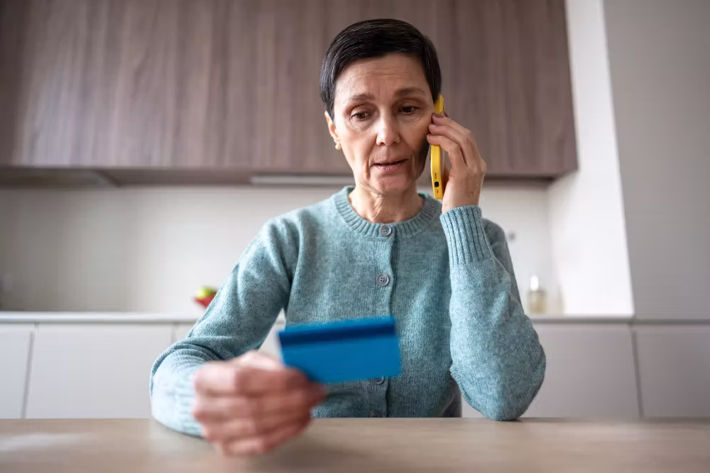 elder-financial-abuse-what-to-be-aware-of An older woman on the phone, looking down at a credit card.